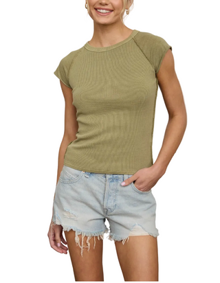 Woman wearing a light olive green top and denim shorts in a laundry room.
