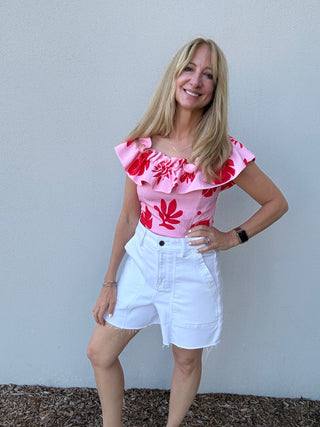 woman against a white wall Ruffle in a Strapless Pink and Red Top and white denim shorts