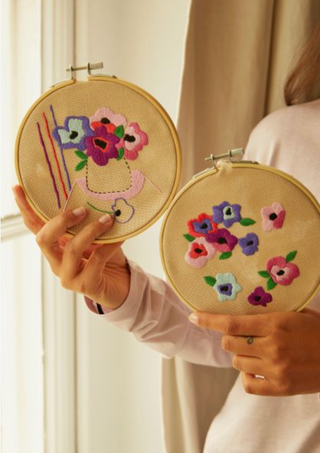 Two embroidered hoops with floral designs held by a person.