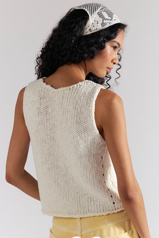 Woman wearing a beige knitted sleeveless top and yellow pants against a plain background