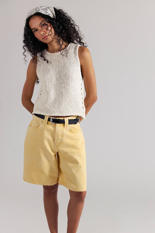 Woman wearing a white sleeveless top and yellow shorts on a plain background