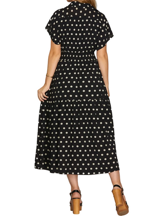 A woman wearing a black midi dress with a white polka dot pattern, shown from the back against a light gray studio background.