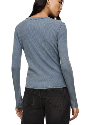 A woman shown from the back wearing a light blue ribbed long-sleeve top and dark gray jeans against a plain beige studio background.