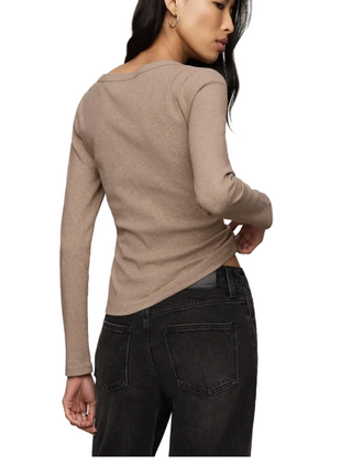 A woman shown from the back wearing a fitted, long-sleeve knit top in a warm taupe-beige color, paired with dark gray jeans, against a plain light beige studio background.