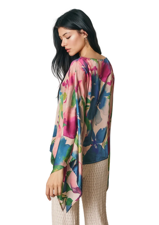 A woman wearing a colorful floral print long-sleeve top and textured beige pants, photographed against a solid white background.