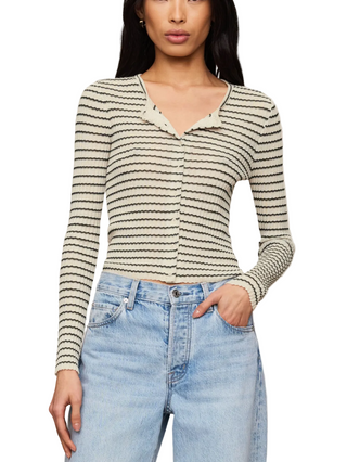 A woman wearing a fitted long-sleeve knit top with thin horizontal black stripes on an off-white base, paired with light-wash blue jeans, against a plain beige studio background.