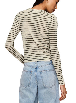 A woman shown from the back wearing a fitted long-sleeve knit top with thin horizontal black stripes on an off-white base, paired with light blue jeans, against a plain beige studio background.