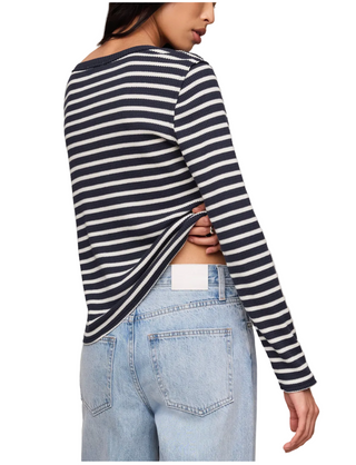 A woman wearing a navy and white horizontally striped long-sleeve crop top with a side slit, paired with light blue jeans, shown from a rear three-quarter angle against a plain beige background.