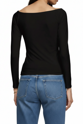 A woman shown from the back wearing a black long-sleeve off-the-shoulder top and dark gray jeans against a plain light beige studio background.