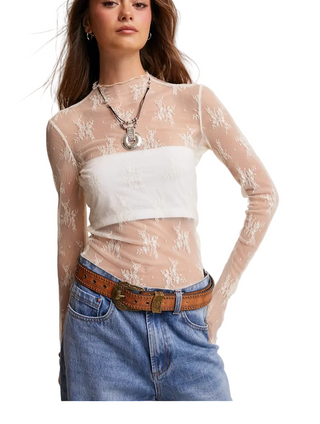 A woman wearing a sheer ivory  long-sleeve top with floral lace embroidery over a bandeau-style underlayer, paired with a a denim jeans