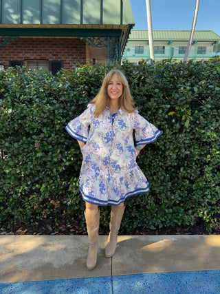 Woman in a floral dress standing in front of a hedge