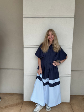 Woman wearing a navy and white dress standing against a beige wall.