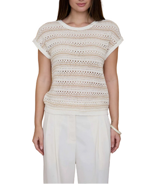 Woman wearing a beige crochet top and white pants against a striped background