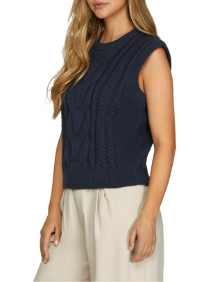 Woman wearing a navy sleeveless knitted top against a plain background