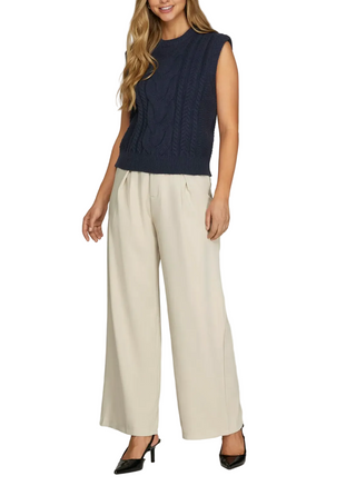 Woman wearing a navy sleeveless top and beige wide-leg pants on a plain background