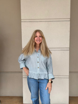 Woman wearing a striped shirt and jeans standing against a plain wall.