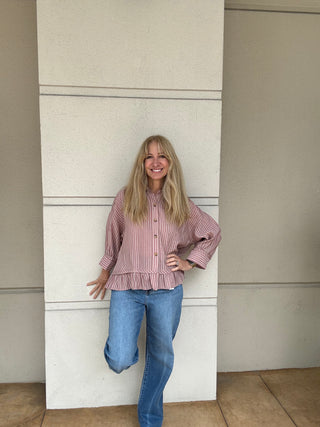 Woman wearing a red and white striped shirt and blue jeans standing against a beige wall.