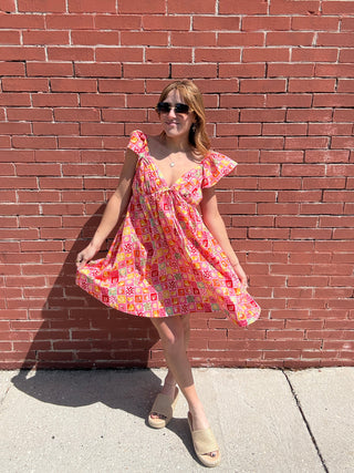 Person wearing a colorful dress standing on a brick sidewalk.