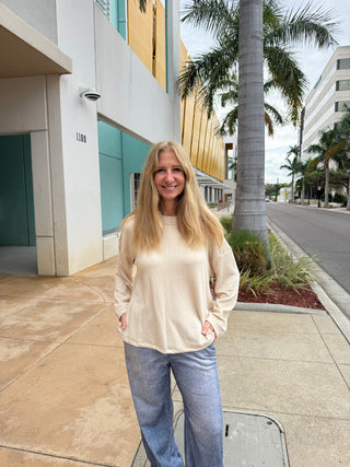 Woman standing on a sidewalk with palm trees and buildings in the background. wearing Sweatpant Jeans