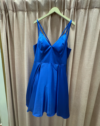 a formal satin mini dress in the color royal blue against a cream curtain background 