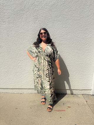 Woman wearing a patterned dress standing against a white wall.