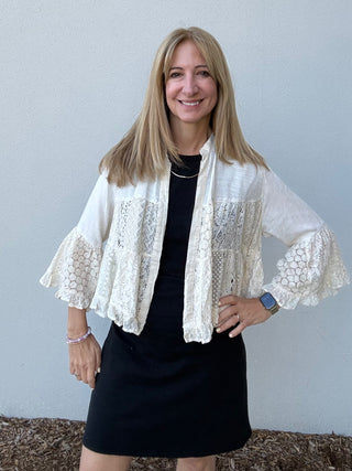 Woman wearing a white lace top over a black dress against a plain background