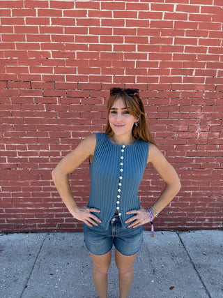 Person standing on a red brick sidewalk wearing a blue dress with white buttons.