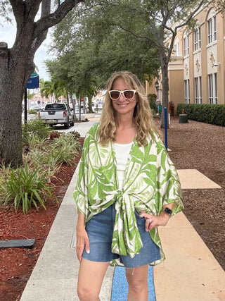 Woman wearing a green and white patterned jacket on a sidewalk with trees and buildings in the background.