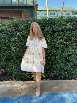 Woman in a white floral dress standing in front of green bushes