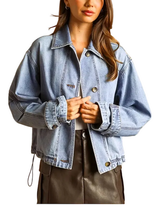 A woman wearing a light blue cropped denim jacket with front button closures, shown against a warm tan studio background. The image includes small thumbnail views at the lower left and a text callout describing the jacket's design and construction details.