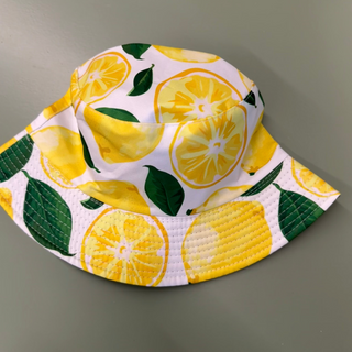 bucket hat with lemons on white background with some green leaves