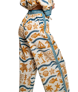 A person wearing high-waisted wide-leg pants with a nautical print in orange and blue on a cream background, shown from the waist down against a plain light gray studio backdrop.