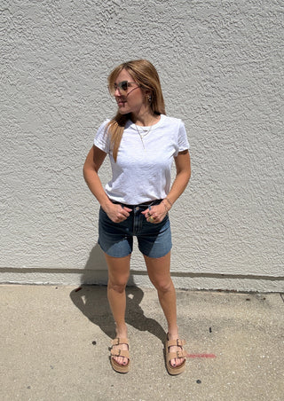 Person standing on a sidewalk with a white wall in the background