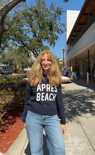 Woman wearing a sweatshirt with 'Apres Beach' text on a sidewalk.