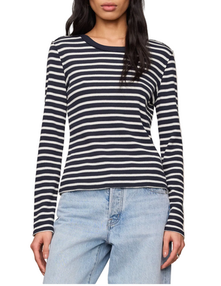 A woman wearing a navy and white horizontally striped long-sleeve knit top with light-wash blue jeans, shown from the lips down against a plain beige studio background.