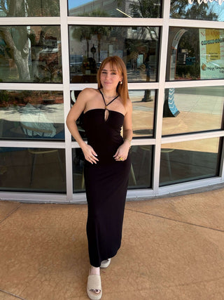Woman in a black dress standing in front of a building with large glass windows.