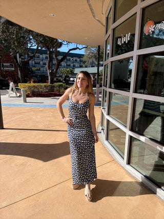 Woman in a patterned dress standing on a sidewalk with a building in the background