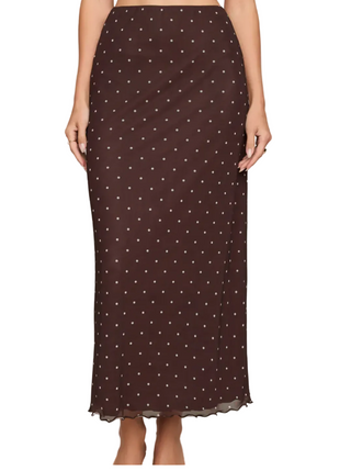 A woman wearing a dark brown midi skirt with a white polka dot pattern, shown from the waist down against a light beige studio background.