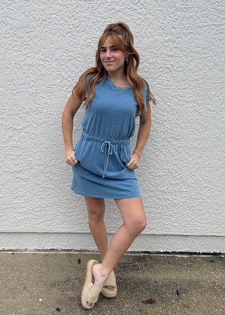 Girl in a denim dress standing against a white wall