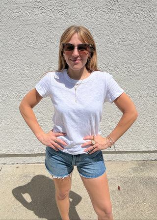 Person wearing a white t-shirt and denim shorts standing against a light gray wall.