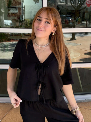 Woman in a black outfit standing in front of a glass window with reflections.