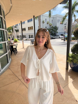 Woman in a white dress standing on a sidewalk with buildings and trees in the background