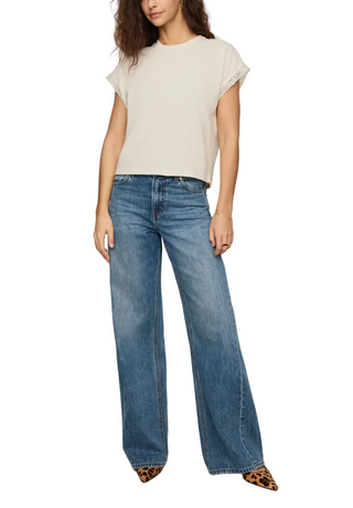 A model wearing a cream short-sleeve top and wide-leg blue jeans, paired with leopard-print pointed shoes, against a plain beige studio background.
