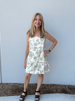 Woman wearing a floral dress standing against a plain wall.
