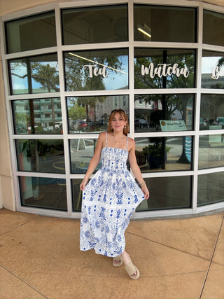 Person wearing a blue floral dress standing in front of a glass building entrance.