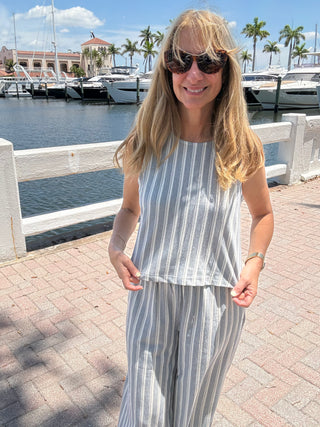 Woman in a striped outfit standing by a waterfront with boats and palm trees in the background.