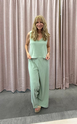 Woman wearing a mint green outfit standing in front of a pink curtain.