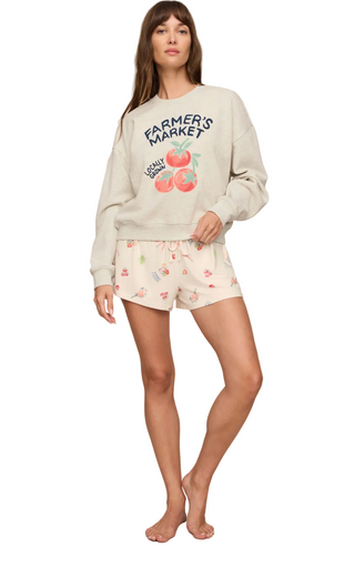 A woman modeling a light beige crewneck sweatshirt with a 'FARMER'S MARKET' graphic and matching floral print shorts against a solid beige background.