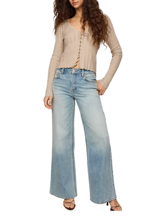 A model wearing a beige button-up cardigan and light blue wide-leg jeans, standing against a plain beige studio background.