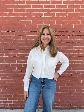 Woman wearing a white shirt and blue jeans standing against a red brick wall.